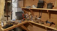 Wide view of workbench area in basement showing hand tools and hardware arranged on wooden shelves and work surfaces.