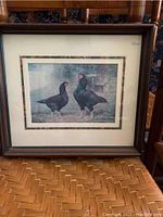 Framed bird art print showing two black birds with red markings, dark wood frame with cream and decorative patterned matting.