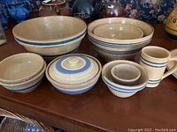 Overview of lot showing seven yellow ware pieces including bowls of various sizes and a mug all with blue band decoration.