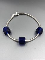 Sterling silver snake chain bracelet with three large cobalt blue octagonal beads placed spaced on the bracelet, shown from side view on dark gray surface.