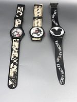 Three Mickey Mouse themed wristwatches laid out flat showing faces and straps.