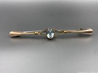 Full front view of the gold bar brooch with central aquamarine gemstone, showing the overall design and length.