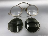 Top view showing one pair of antique spectacles with clear lenses above and one pair of clip-on sunglasses with dark lenses below.