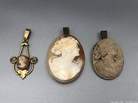 Three cameo pendants arranged side by side on a flat surface showing their varying sizes and materials.