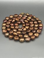 Full view of the chocolate brown pearl necklace coiled on a grey surface, showing the overall condition and color of the pearls.