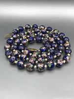 Close-up showing gold-tone filigree floral designs on dark blue cloisonné beads of the necklace.