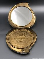 Open view showing mirror and decorative powder chamber inside the round gold-tone compact