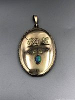 Full front view of the gold filled oval locket showing embossed rose and leaf design with central opal cabochon.