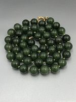 Top-down view of the coiled jade bead necklace highlighting the polished round beads and gold-tone clasp.