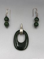 Single image of the jade pendant and earrings set arranged flat on a gray background, showing the pendant's size and earring details.