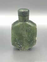 Front view of octagonal green jade snuff bottle with carved floral and branch motif and round jade stopper on top.