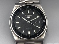 Close-up front view showing the black dial with silver hour markers, hands, and day-date window, with visible scratches on the crystal and dial surface.