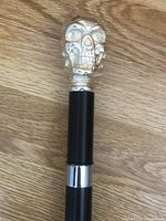 Close-up of silver skull handle atop black cane with silver ring below the handle.