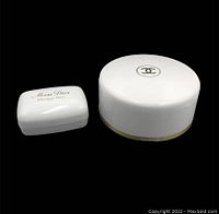 Photo showing closed white ceramic soap dish with gold 'Miss Dior Christian Dior' logo and white round Chanel bath powder container with gold trim and Chanel logo on lid.