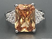 Front view of the sterling silver ring with large rectangular orange gemstone and side clear stones on a gray background.