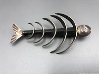 Side and top angle showing the brooch shape, fish head, ribs, and tail fin in sterling silver with polished finish.