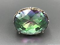 Close-up front view of the large oval mystic topaz stone showing green and purple hues with a detailed faceted surface in a sterling silver setting.