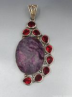 Front view of sterling silver pendant with large oval purple stone and surrounding red teardrop stones.