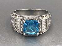 Front view of sterling silver ring with large square blue stone and surrounding clear stones.