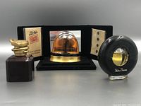 Front view of three vintage perfume bottles including Jean Paul Gaultier, amber bottle in black tri-fold display, and black circular Paloma Picasso bottle.