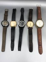 Front view of five vintage wristwatches aligned side by side showing face details and straps