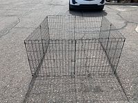 Front view of the 8-panel metal pet pen showing gate panel locked, forming a rectangular enclosure on asphalt surface.