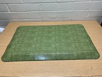Overhead view of the green anti fatigue mat on a wooden table, showing the textured surface and rounded edges.