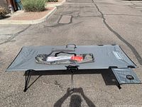 Gray Coleman Pack Away cot fully opened showing full length and attached cup holder pocket on one end.