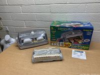 Clear plastic and gray base EZLaminator laminator with laminating cartridge sealed alongside original colorful product box and instruction sheet displayed on a table.