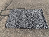 Top-down view of gray and black shaggy flokati area rug on pavement to show full front surface and texture.