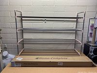 Image of assembled four-tier Home Complete shoe rack standing on its packaging box against a wall.