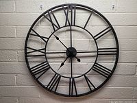 Front view of the large metal wall clock mounted on a wall, showing Roman numerals and clock hands.