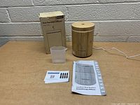 Full lot showing InnoGear bamboo diffuser, measuring cup, instruction manual, warranty card, and original box on a table against a brick wall background.