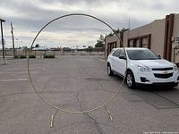 Frontal view of the Kusamue large circular balloon arch frame standing in parking lot with a white car behind it showing the scale and the full round shape of the frame.