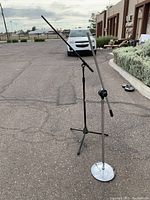 Two microphone stands outdoors on pavement, showing full height and boom arms.