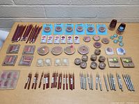 Top-down photo showing the full lot arranged on a wooden surface against a brick wall, including pencils, compacts, and jars of makeup.