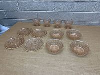 Top front view of 12 pink vintage glass items arranged on a beige surface, showing the pedestal bowls at the back and plates and bowls in front