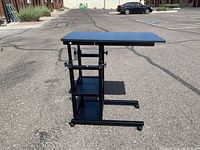Front-side view of black adjustable height rolling computer desk with two shelves and caster wheels