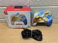 View of the Nintendo Switch controller and its original box, showing the Pikachu-themed controller with an attached cable.