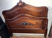 Front view of antique full-size walnut wood bed showing carved headboard and footboard with ornate detailed moldings and smooth panels.