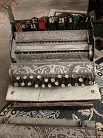 Front view of antique cash register with rows of numbered keys and metal ornate casing indicating various denominations.
