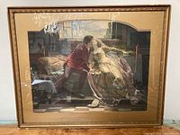 Full view of framed antique print showing a man and woman seated on a bed sharing a kiss, glass and frame visible reflecting light.