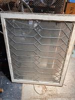 Full view of antique lead glass window showing geometric leaded diamond pattern and wooden frame.