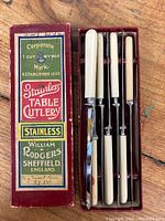 Original red box with colorful label reading 'Stainless Table Cutlery William Rodgers Sheffield England' alongside four utensils with ivory-colored handles and stainless steel blades inside original slots.