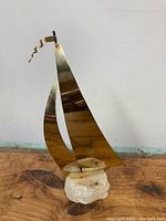 Front view showing brass sails, boat, and white stone base with signature visible on base.