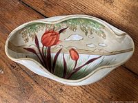 Top view of the hand painted oval ceramic dish showing red tulips with green leaves and a background of beige and green tones with clouds.