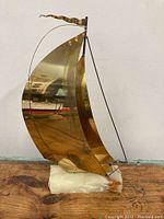 Full view of large brass sailboat sculpture showing front with two large sails and a flag at the top mounted on a polished stone base.