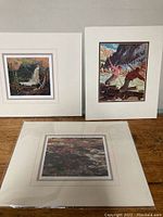 Three matted Group of Seven prints showing landscape scenes placed on a wooden floor