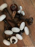 Overview of the antique porcelain door knobs on wooden surface showing multiple white oval knobs and some brown glazed ones.