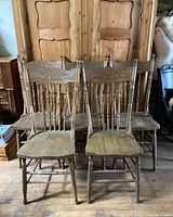 Five solid wood antique chairs with carved pressback backs arranged together in room. Visible wear and missing screws on hip rests.